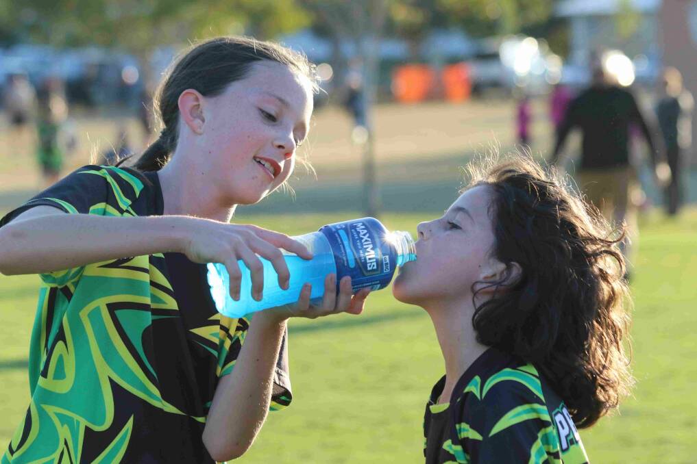 Sharing is caring: Big sister Ella Hicks helps little sister TJ cool off with a mouthful of her sports drink. Photo: John Warlters