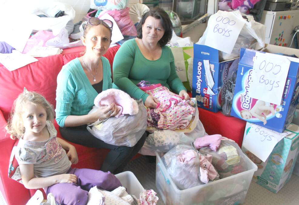 COMMUNITY-MINDED: Angela Hampton and Cindy Fox have started a children's clothes swapping initiative. Helping to sort donations is four-year-old Isabella Hampton. Photo: Cheryl Goodenough
