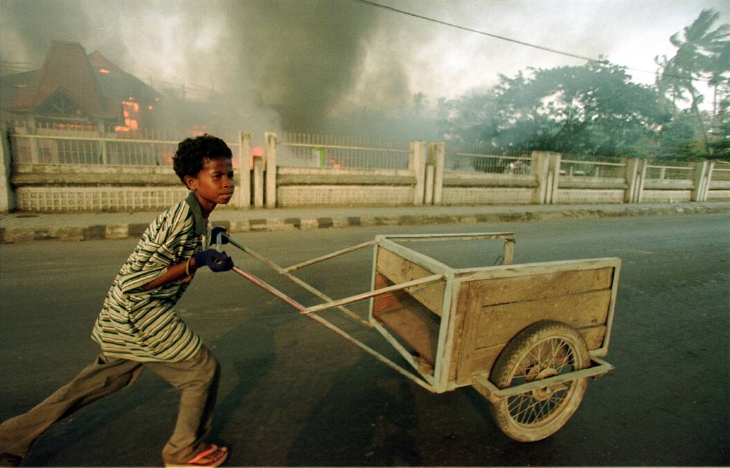 Fires on the streets of Dili, as a local East Timorese boy runs by, September 1999. Picture: Getty Images