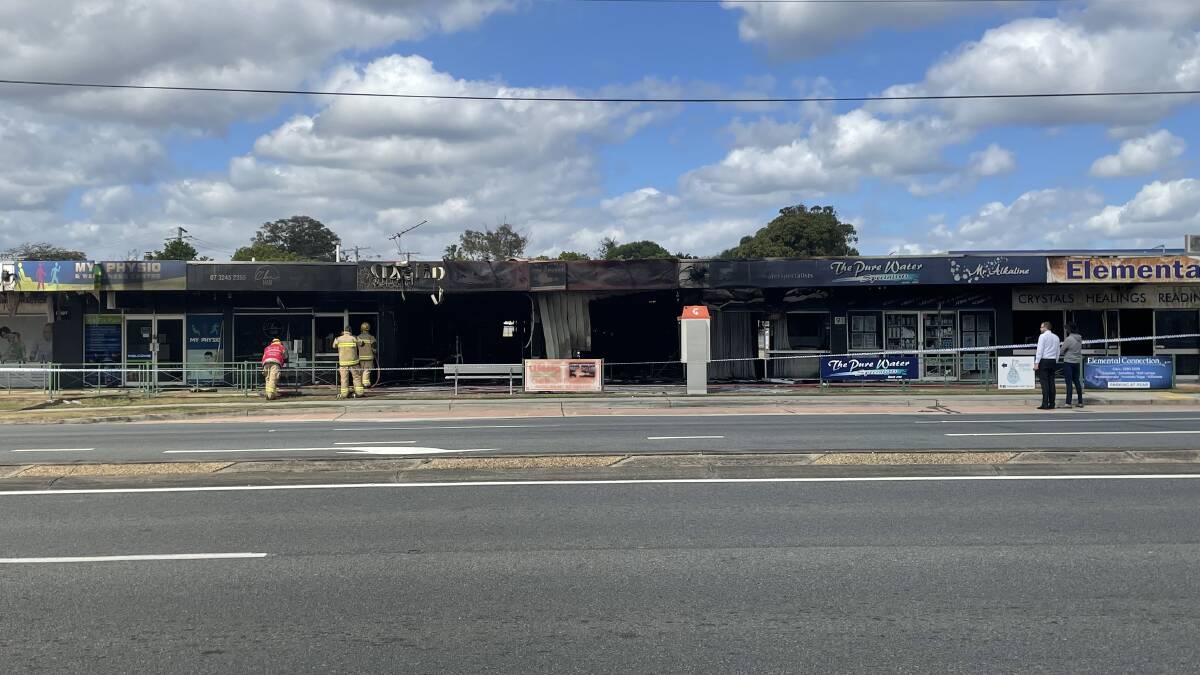 Firies and police take a closer look at the damage caused by a fire that tore through shops on Old Cleveland Bay Road, Capalaba this morning.