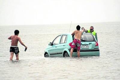 Japanese tourists try pushing their rented car out of the mud as the tide comes in.