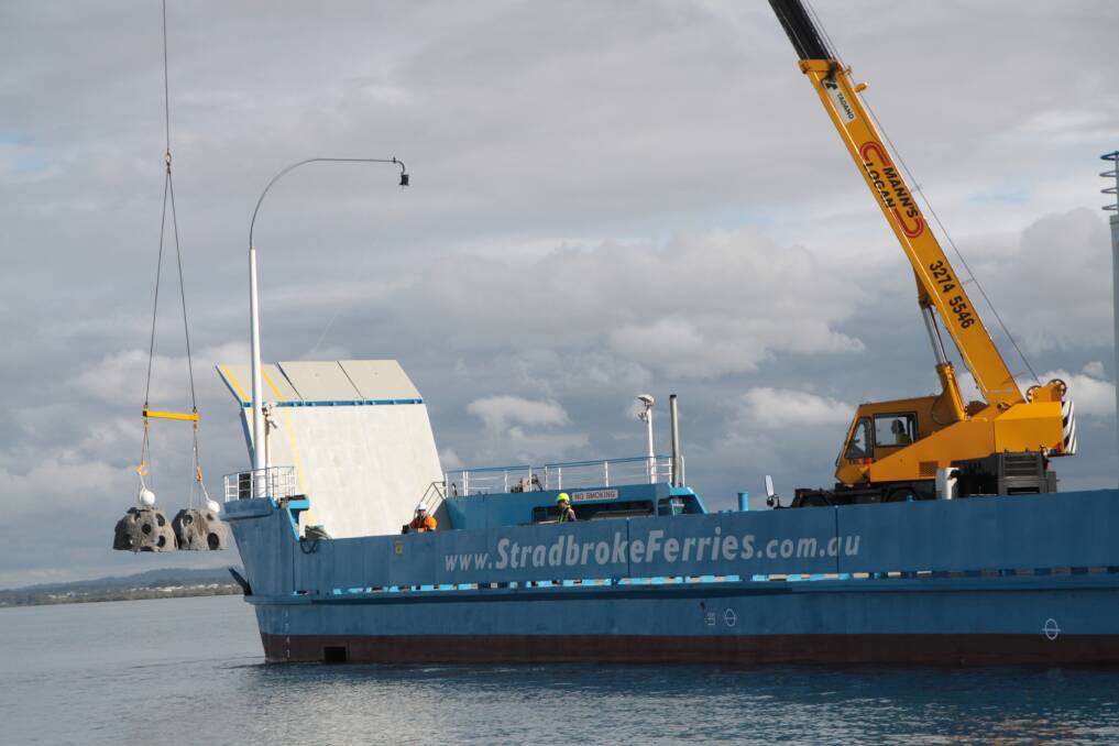 A large crane on the deck of a Stradbroke Ferries barge hoists the concrete balls into the water off Peel Island. Photo: Chris McCormack